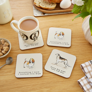 Set of coasters with dog illustrations and text on a wooden table with a mug of tea.