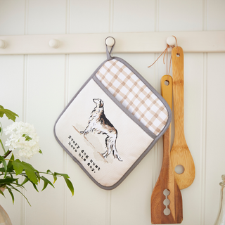 Potholder with dog illustration and checkered pattern, wooden spatula, and white flowers on a light wooden background