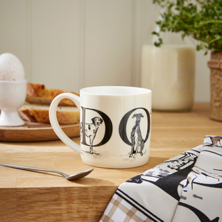 White mug with dog design on a wooden table with a plant and bread in the background