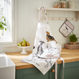 Kitchen counter with a white apron featuring dog illustrations, a pot holder, and pears on a wooden surface.