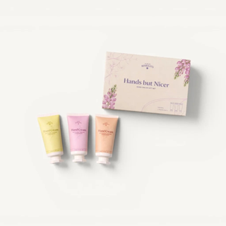 A hand cream gift set featuring three squeeze tubes in yellow, pink, and peach next to their matching floral-patterned packaging box on a clean white background.