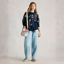 Load image into Gallery viewer, Woman wearing a floral embroidered sweater and light blue jeans against a plain background
