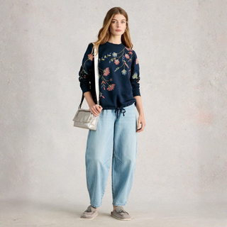 Woman wearing a floral embroidered sweater and light blue jeans against a plain background