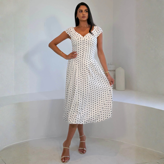 Woman wearing a white dress with black polka dots in a minimalistic setting