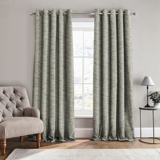 Gray textured curtains hanging in a living room with a sofa and lamp.