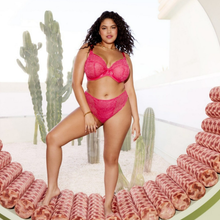 Load image into Gallery viewer, A woman modeling a bright pink lace bra and matching high-waisted bikini bottoms, standing on a circular pink platform with cacti in a bright, modern setting.
