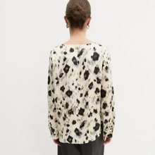Load image into Gallery viewer, A woman viewed from the back wearing a long-sleeve blouse with a black, gray, and beige abstract spotted pattern on a cream background, paired with dark gray trousers, against a plain white studio background.
