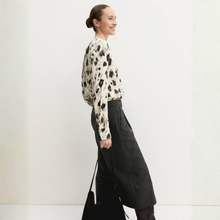 Load image into Gallery viewer, A woman wearing a cream long-sleeve blouse with a black abstract print and black wide-leg trousers, standing against a plain white studio background and holding a black tote bag.

