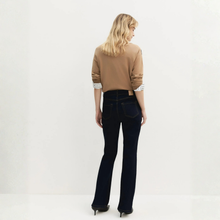 Load image into Gallery viewer, A woman is shown from behind wearing dark blue flare jeans, a tan sweater with striped cuffs, and black heels, photographed against a plain white studio background.

