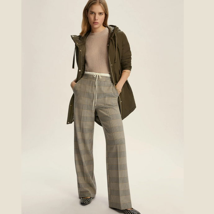 Woman wearing a green coat and plaid pants on a plain background