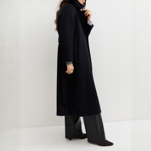 Load image into Gallery viewer, A woman wearing a long navy coat, wide-leg dark trousers, and pointed shoes, photographed in a minimalist white studio setting.
