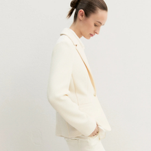Load image into Gallery viewer, A woman wearing a structured cream-colored blazer and matching trousers, shown in profile against a plain light background.
