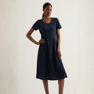 Woman wearing a navy dress with white polka dots on a plain background