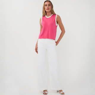 Woman wearing a pink sleeveless top and white pants on a plain background