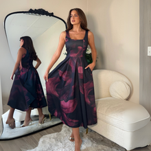 Load image into Gallery viewer, Woman in a dark floral dress standing in front of a mirror in an elegant room.
