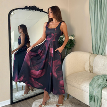 Load image into Gallery viewer, Woman in a dark floral dress standing in front of a mirror in a living room.

