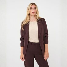 Load image into Gallery viewer, A blonde model wearing a dark brown tailored blazer and matching trousers over a cream knit top, standing against a light gray studio background.
