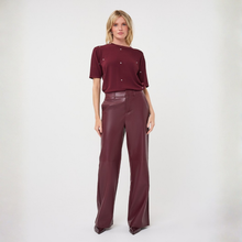 Load image into Gallery viewer, A woman stands against a plain light gray studio background wearing a short-sleeve burgundy top with small metallic embellishments and matching wide-leg burgundy pants.
