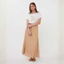 Load image into Gallery viewer, Woman wearing a white t-shirt with a graphic design and a beige long skirt on a white background
