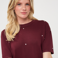 Load image into Gallery viewer, A close-up of a woman wearing a short-sleeve crewneck top in burgundy with small silver stud embellishments on the chest and shoulders, set against a plain light gray background.

