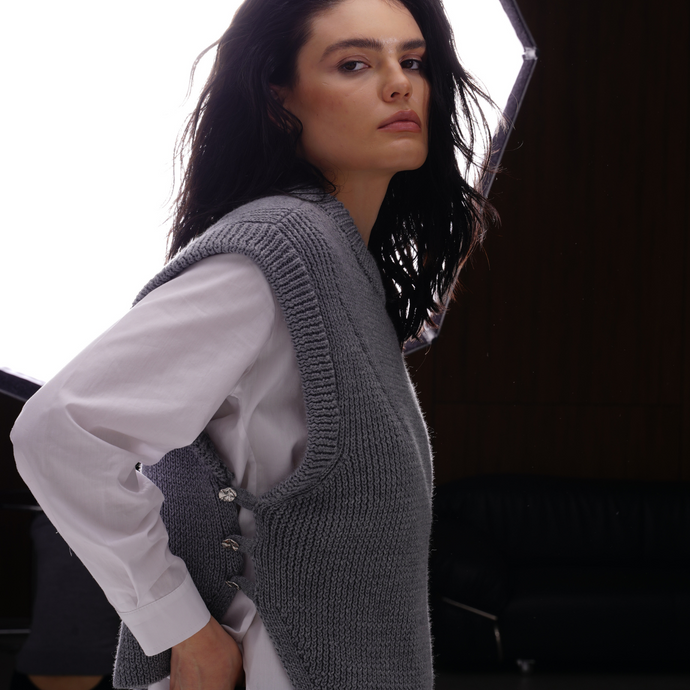 Woman wearing a gray knitted vest over a white shirt with a blurred background