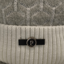 Load image into Gallery viewer, A close-up of a chunky knitted beanie featuring a bold white and grey geometric pattern, finished with a black and silver logo displaying the letter “P”.
