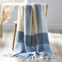 Load image into Gallery viewer, Blue and beige plaid blanket draped over a wooden chair in a room with a light gray wall and wooden floor.
