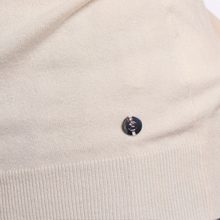 Load image into Gallery viewer, Close-up of a cream-colored knit garment featuring a small, round black button with a silver-toned skull-and-crossbones motif, set against a white background.

