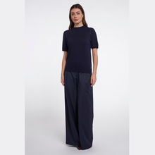 Load image into Gallery viewer, A woman modeling a navy blue short-sleeve knit top and matching wide-leg trousers against a plain light gray studio background.
