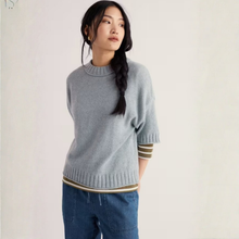 Load image into Gallery viewer, A woman wearing a light gray knit sweater with striped trim at the cuffs and hem, paired with blue jeans, photographed against a plain off-white studio background.
