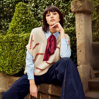 Woman sitting outdoors wearing a patterned vest and red scarf