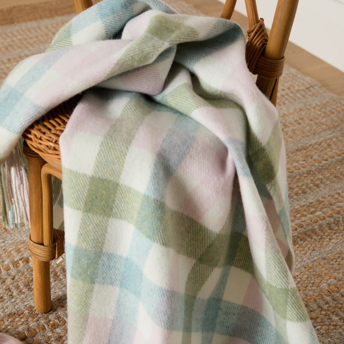 Plaid blanket draped over a wicker chair on a carpeted floor