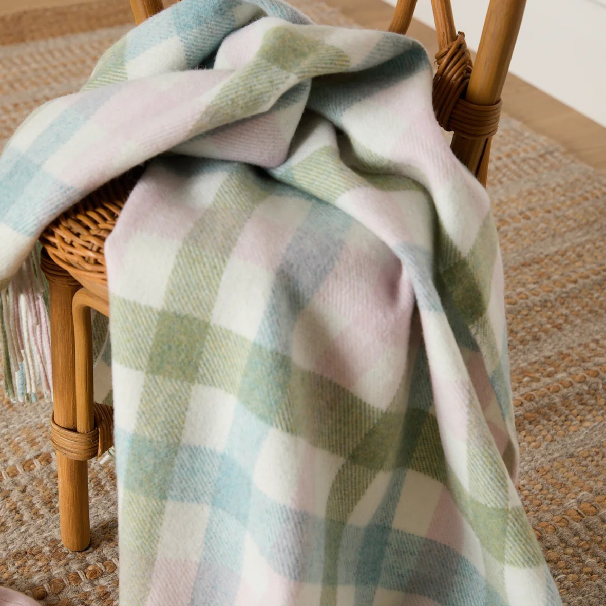 Plaid blanket draped over a wicker chair on a carpeted floor
