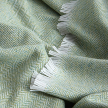 Load image into Gallery viewer, A close-up of a woven textile with a pale sage green and white herringbone pattern and white fringe tassels.
