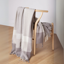 Load image into Gallery viewer, Plaid blanket draped over a wooden chair on a light wood floor.
