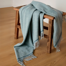 Load image into Gallery viewer, Light blue throw blanket with fringes draped over a wooden stool on a wooden floor.
