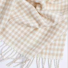 Load image into Gallery viewer, A close-up of a cream and beige checkered scarf with fringed edges, draped to show its soft texture and pattern.
