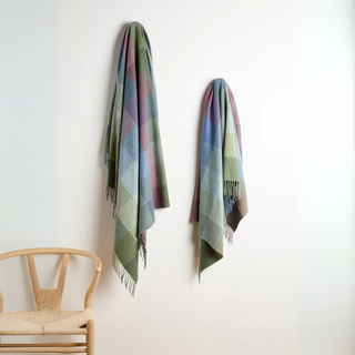Two plaid scarves hanging on a white wall with a wooden chair below.