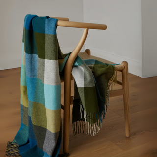 Plaid blanket draped over a wooden chair on a wooden floor.