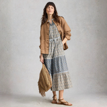 Load image into Gallery viewer, Woman wearing a patterned dress with a brown jacket and holding a fringed bag against a plain background
