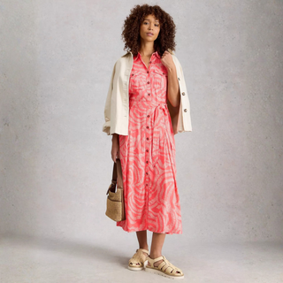 Woman wearing a pink dress with a beige jacket against a gray background