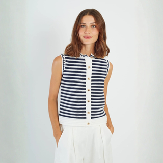 Woman wearing a navy and white striped sleeveless top with buttons on a plain background