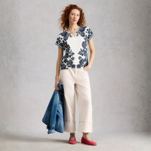 Load image into Gallery viewer, Woman wearing a floral blouse and beige pants, holding a denim jacket against a gray background
