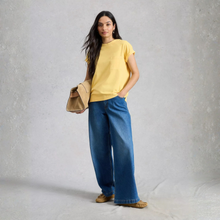 Load image into Gallery viewer, Woman wearing a yellow top and blue jeans holding a beige bag against a gray background
