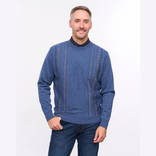 A man wearing a blue crewneck sweater with vertical textured stripes and dark blue jeans, standing against a plain white studio background.