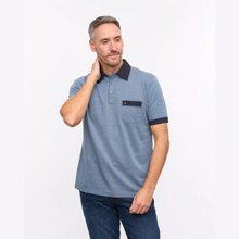Load image into Gallery viewer, A man wearing a heathered blue polo shirt with a dark navy collar, sleeve trim, and chest pocket, paired with dark blue jeans, against a plain white studio background.
