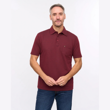 Load image into Gallery viewer, A man wearing a short-sleeve polo shirt in maroon with a small embroidered logo on the chest pocket, paired with blue jeans, standing against a plain white studio background.
