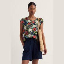 Load image into Gallery viewer, Woman wearing a floral top and navy shorts with a beige bag on a light background
