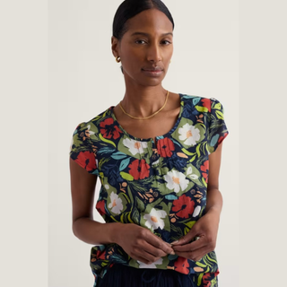 Woman wearing a colorful floral top against a plain background