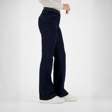 Load image into Gallery viewer, A person shown from the waist down wearing dark navy wide-leg jeans, a white long-sleeve top, and white sneakers against a clean white studio background.
